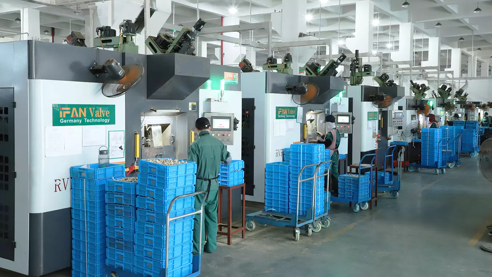 Rows of CNC machining centres turning brass valve bodies, with finished blanks stacked in crates beside each machine