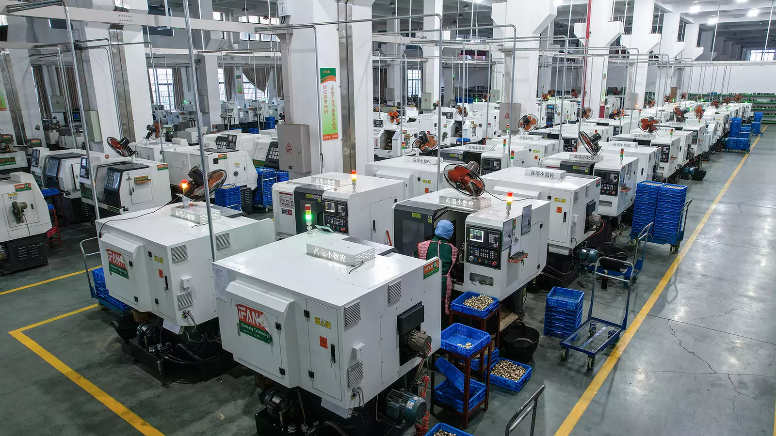 Rows of CNC bar-turning machines producing brass fittings on a pipe fitting factory floor