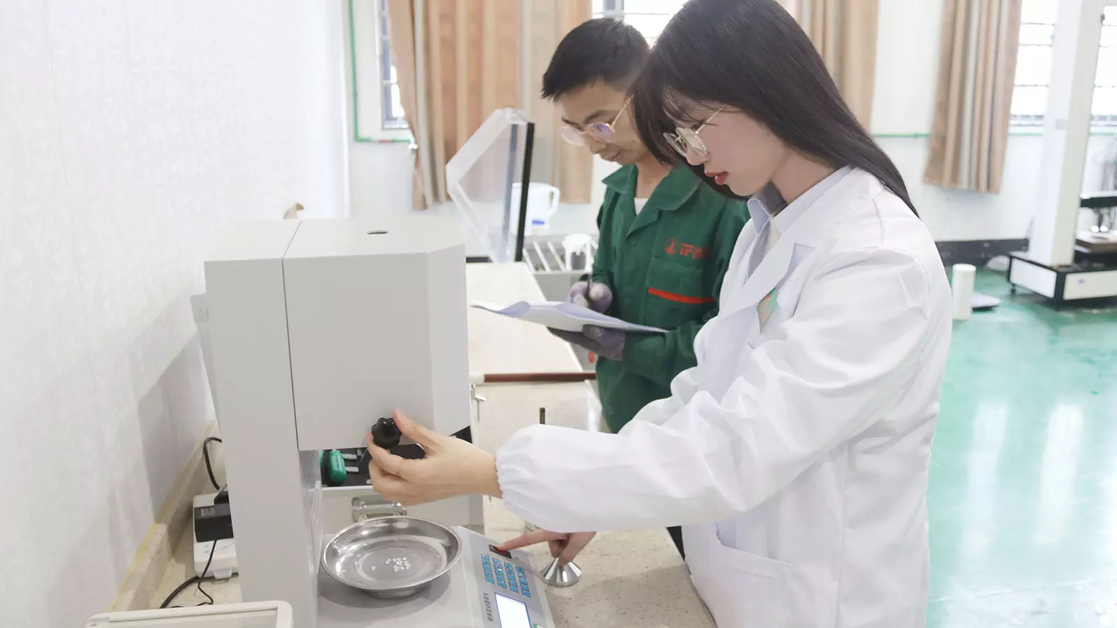 Two technicians in a materials laboratory operating benchtop test equipment for pipe fitting quality control
